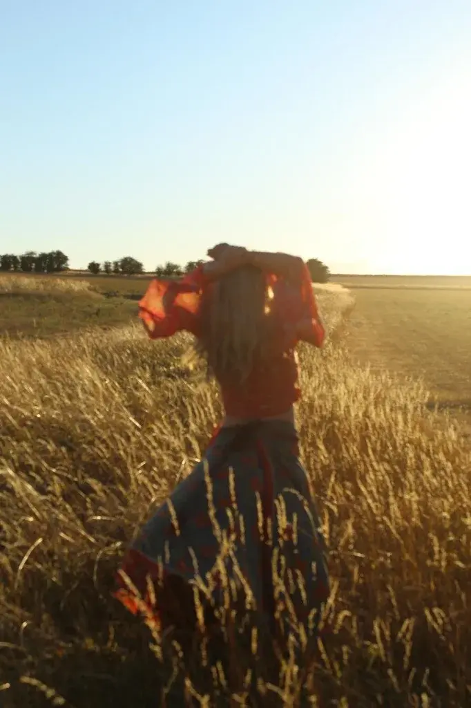 Indiana from behind, arms over her head, in a sunlit field.