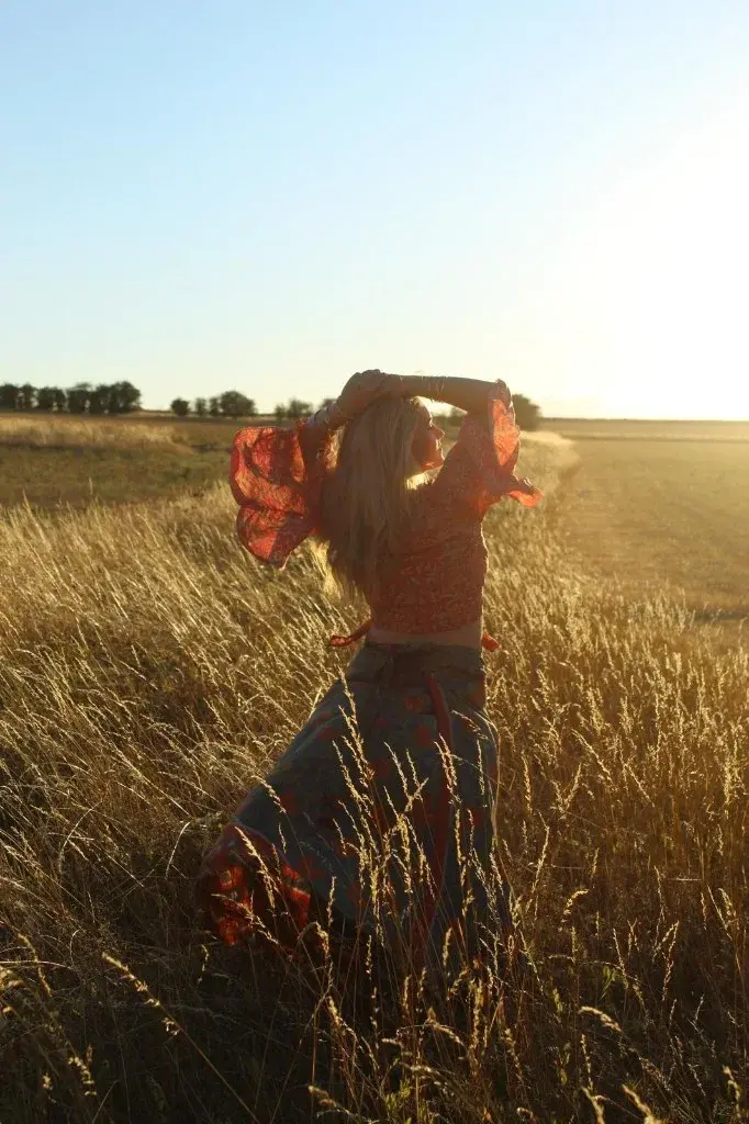 Indiana with her arms over her head in a field at sunset.