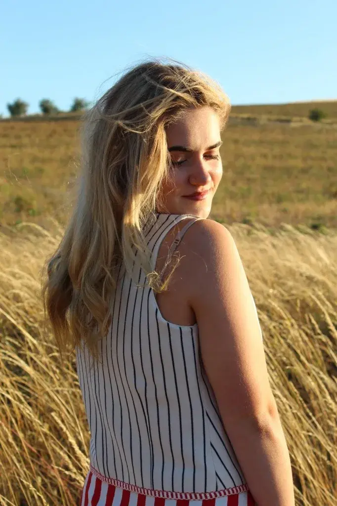 Indiana looking down over her shoulder, eyes closed, in tall grass.