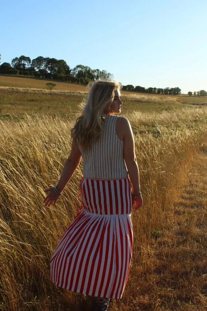 Indiana walking away through long grass in a striped dress.
